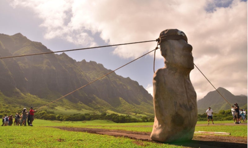 Researchers holding ropes tied to a huge stone statue on Easter Island, trying to replicate the method of moving the statues by 'walking' them.