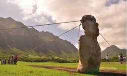 Researchers holding ropes tied to a huge stone statue on Easter Island, trying to replicate the method of moving the statues by 'walking' them.
